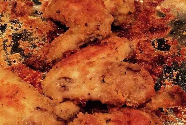 Breaded chicken wings that consist of bread crumbs, Parmesan cheese, garlic powder, melted butter, and a cookie sheet.